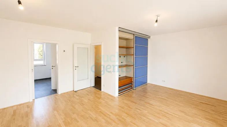 Helles Zimmer mit Holzboden und integriertem Schrank, ideal als Wohn- oder Schlafbereich nutzbar.