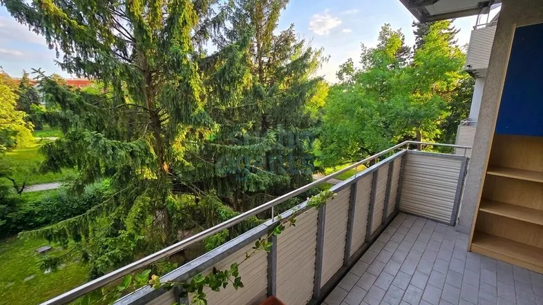 Geräumiger Balkon mit Fliesenboden und weitem Blick ins Grüne, umgeben von hohen Bäumen.