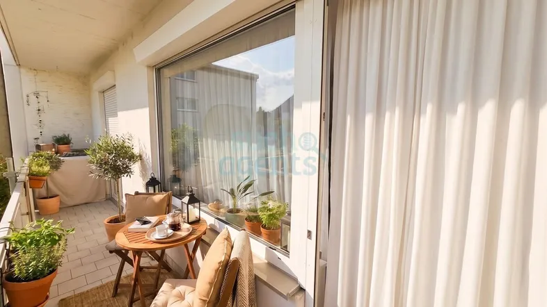 Heller Balkon mit gemütlicher Sitzecke, Pflanzen und Blick auf die Umgebung.