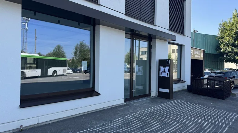 Moderne Geschäftsfassade mit großen Schaufenstern und Eingangsbereich, reflektiert einen vorbeifahrenden Bus.