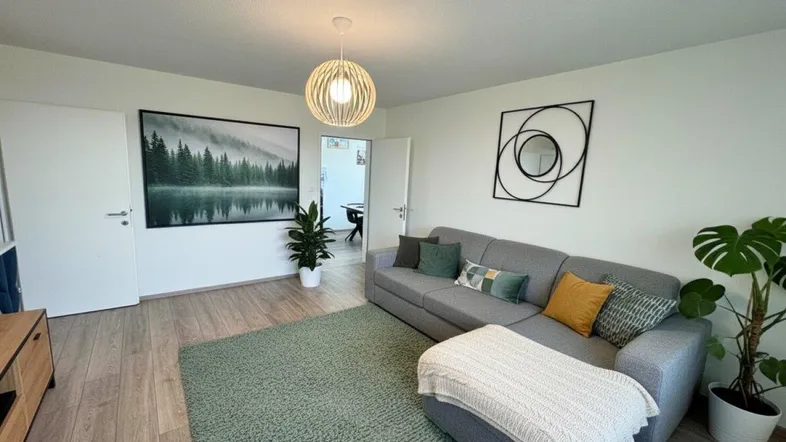 Helles Wohnzimmer mit modernem Sofa, Laminatboden und dekorativen Pflanzen.