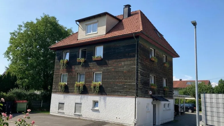 Mehrfamilienhaus mit Holzfassade und Satteldach in sonniger Umgebung.