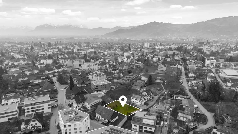 Luftaufnahme einer Stadt mit Bergpanorama, die ein markiertes Grundstück in der Bebauung zeigt.