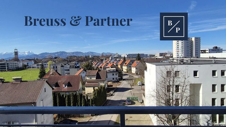 Blick vom Balkon über die Stadt mit Bergen im Hintergrund an einem sonnigen Tag.