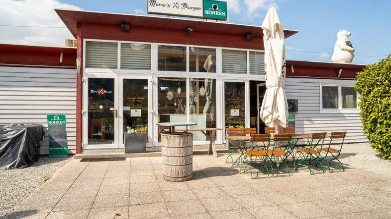 Außenansicht eines Restaurants mit Terrasse und Sonnenschirm, bereit für Gäste an einem sonnigen Tag.