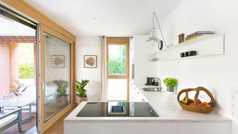 Moderne Küche mit weißer Arbeitsplatte, Induktionskochfeld und Zugang zu einer Terrasse.