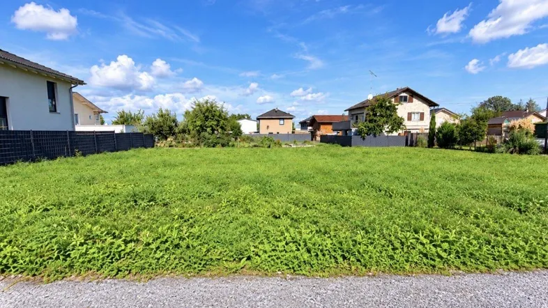 Weitläufiges unbebautes Grundstück in einer Wohngegend unter blauem Himmel mit weißen Wolken.