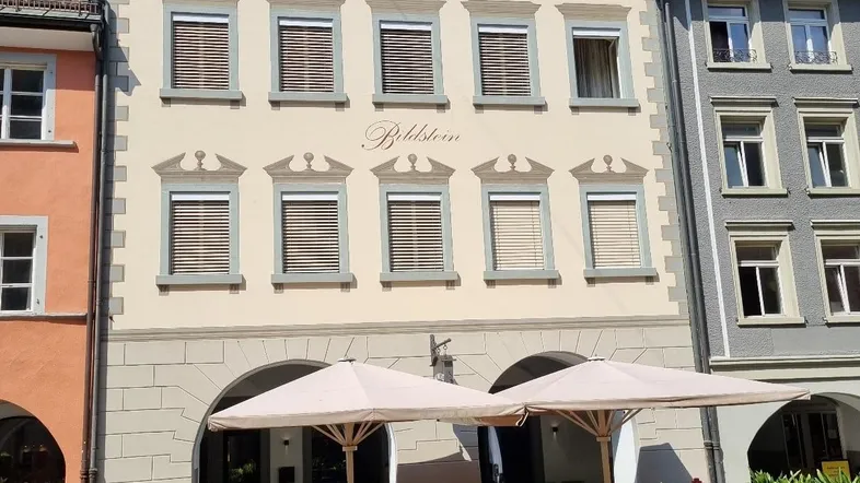 Traditionelles Gebäude mit beiger Fassade, Fensterläden und Gastronomiebereich im Erdgeschoss.