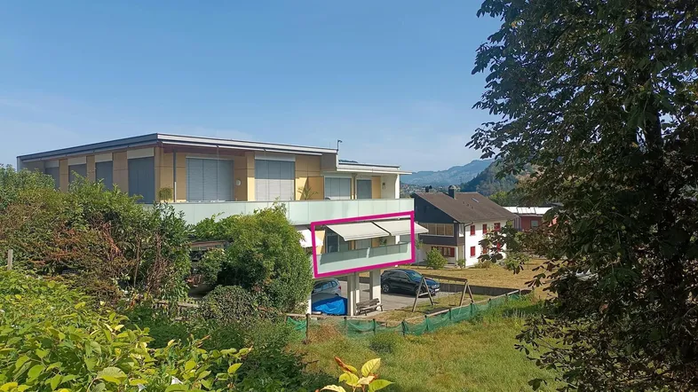 Blick auf das moderne Wohngebäude mit einem sonnigen Balkon und grüner Umgebung.