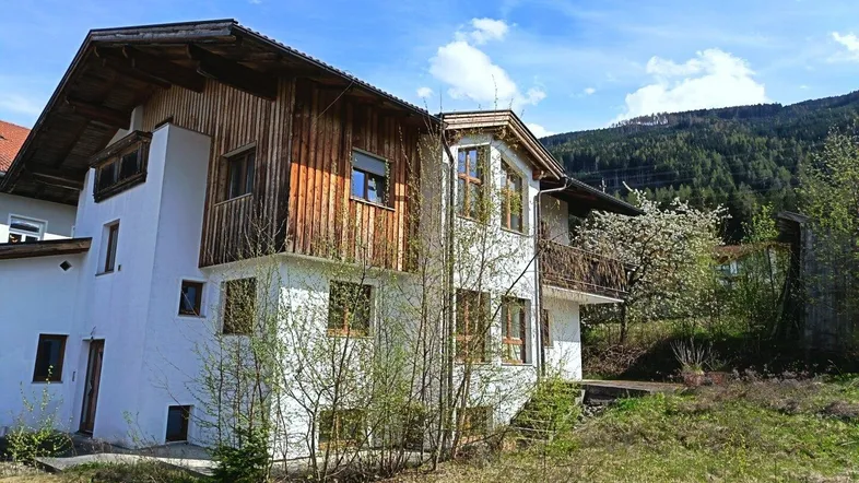 Ländliches Haus mit weißer Fassade, Holzverkleidung und Blick auf die umliegende Berglandschaft.