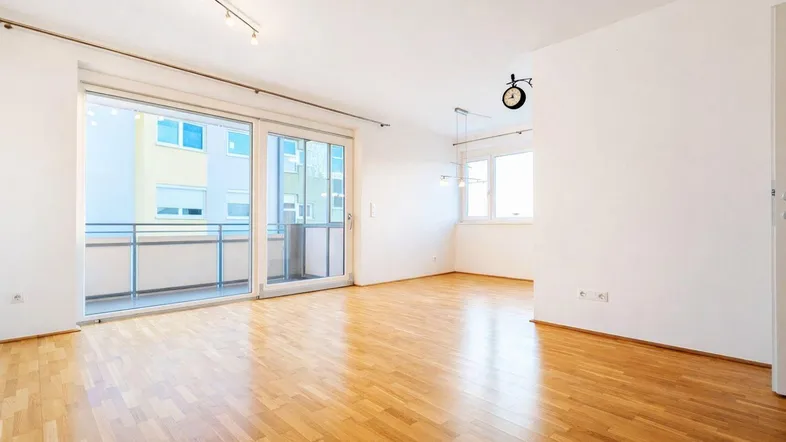 Helles Wohnzimmer mit Parkettboden und Zugang zu einem Balkon, ideal für individuelle Gestaltung.