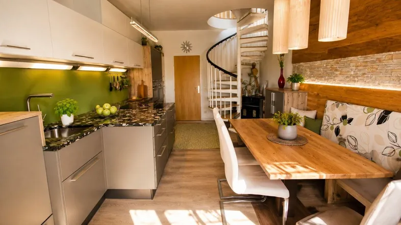 Moderne Wohnküche mit dunkler Arbeitsplatte, Holzelementen und integriertem Essbereich.