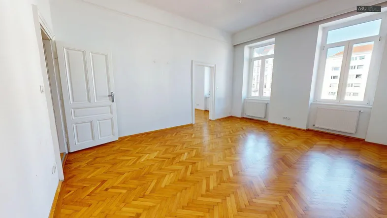 Großes Zimmer mit glänzendem Fischgrätparkett, weißen Wänden und Zugang zu weiteren Räumen.