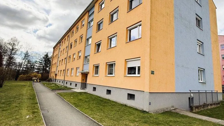 Mehrfamilienhaus mit orange-blauer Fassade und Grünflächen in der Umgebung.