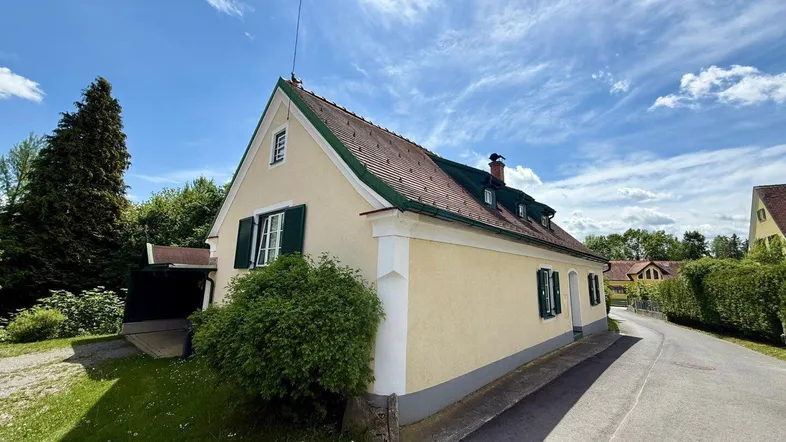 Traditionelles Landhaus mit gelber Fassade, grünen Fensterläden und Satteldach unter blauem Himmel.