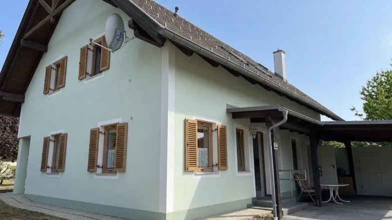 Freistehendes Einfamilienhaus mit hellgrüner Fassade, Satteldach und Holzfensterläden, umgeben von einem gepflegten Garten.