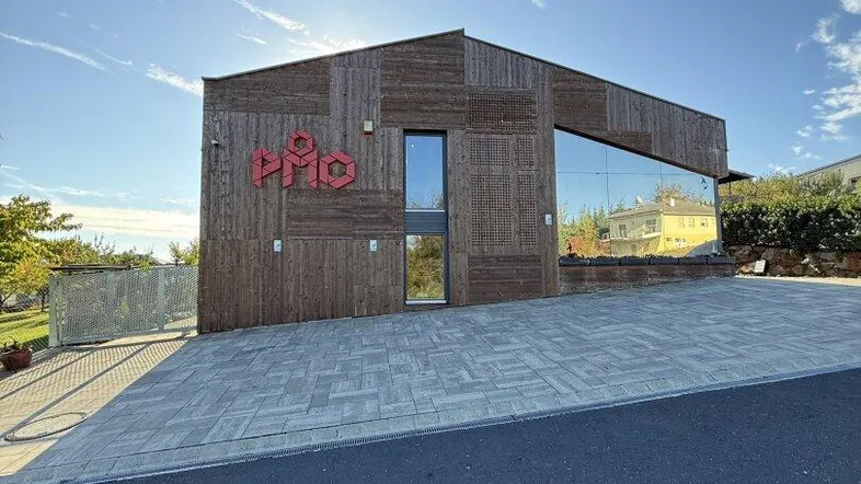 Modernes Gebäude mit Holzfassade und großer Glasfront unter blauem Himmel bei Sonnenschein.