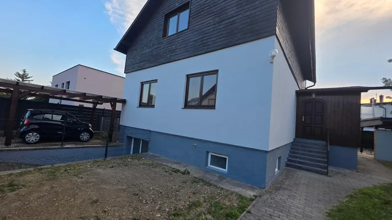 Einfamilienhaus mit weißer und dunkelgrauer Fassade, Carport und gepflastertem Zugang.