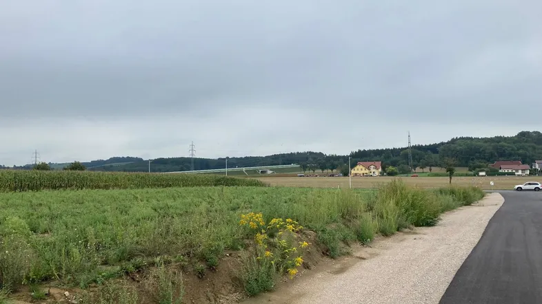 Blick auf weite Felder und ländliche Umgebung mit Häusern in der Ferne unter bewölktem Himmel.