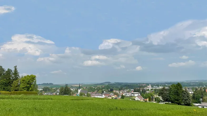 Weitläufige grüne Landschaft mit einem Dorf und Kirche im Hintergrund unter blauem Himmel.