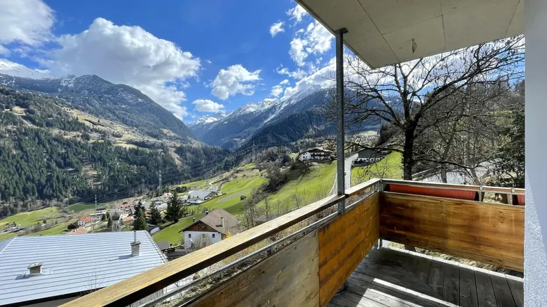 Geräumiger Balkon mit Holzboden und atemberaubendem Blick auf die umliegende Berglandschaft und das Tal.