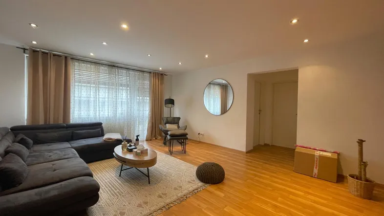 Geräumiges Wohnzimmer mit modernem Sofa, Holzboden und indirekter Deckenbeleuchtung.