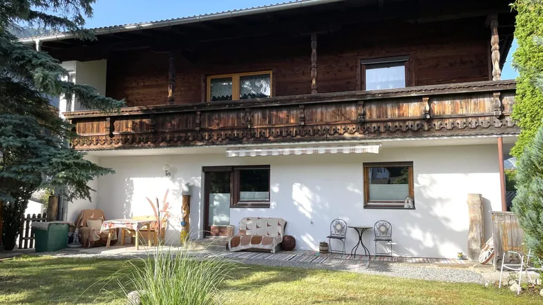 Traditionelles Haus mit Holzbalkon und gepflegtem Gartenbereich mit Sitzgegelegenheiten im Freien.