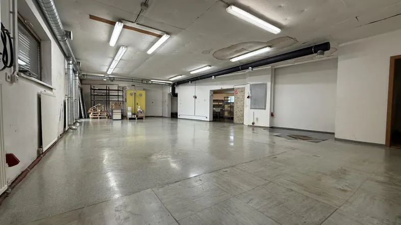 Großer, offener Lagerraum mit Betonboden, sichtbaren Leitungen und Leuchtstoffröhren an der Decke.