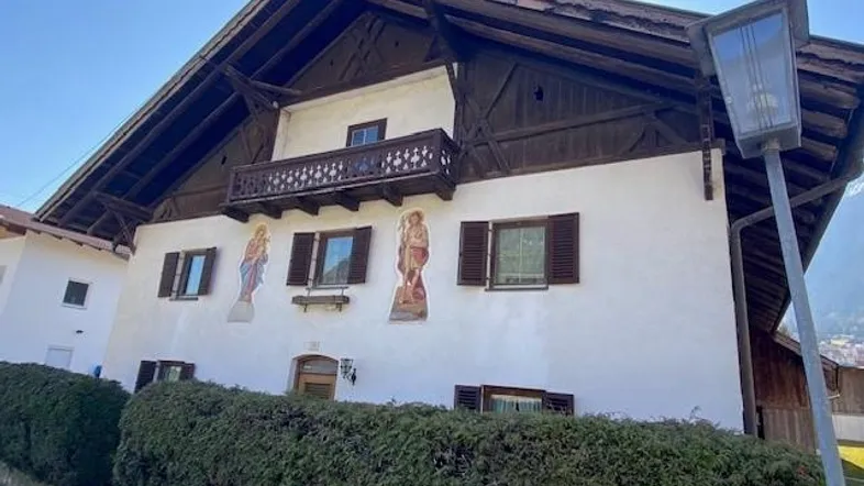 Traditionelles Haus mit Holzbalkonen, bemalter Fassade und grüner Hecke im Vordergrund.