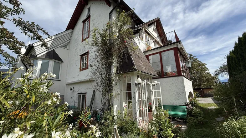 Charmantes Haus mit weißer Fassade, Wintergarten und blühendem Gartenbereich.