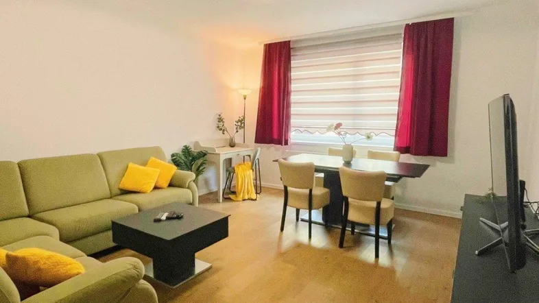 Helles Wohn- und Esszimmer mit Parkettboden, bequemer Couch und modernem Esstisch.