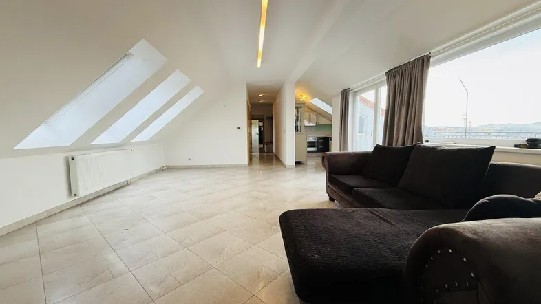 Geräumiges Wohnzimmer mit schrägen Wänden, Fliesenboden und Dachfenstern für Tageslicht.