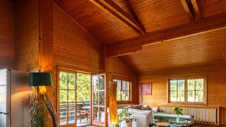 Geräumiges Wohnzimmer im Chalet-Stil mit Holzwänden, hohen Decken und Zugang zur Terrasse.