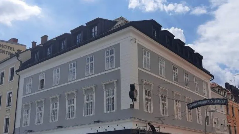 Historisches Gebäude mit frisch renovierter grauer Fassade und weißen Fenstern in einer städtischen Umgebung.