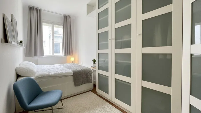 Helles Schlafzimmer mit integriertem Kleiderschrank, bequemen Bett und einem Fenster mit Vorhängen.