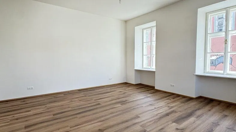 Helles, leeres Zimmer mit neuem Laminatboden und zwei Fenstern, bereit zum Einzug.