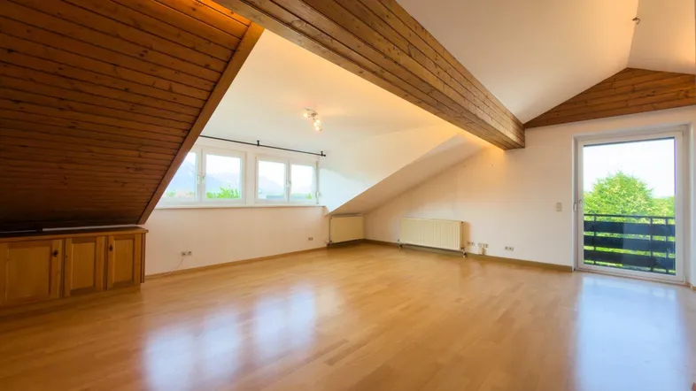 Helles Dachgeschosszimmer mit Holzbalken, Parkettboden und Zugang zu einem kleinen Balkon.