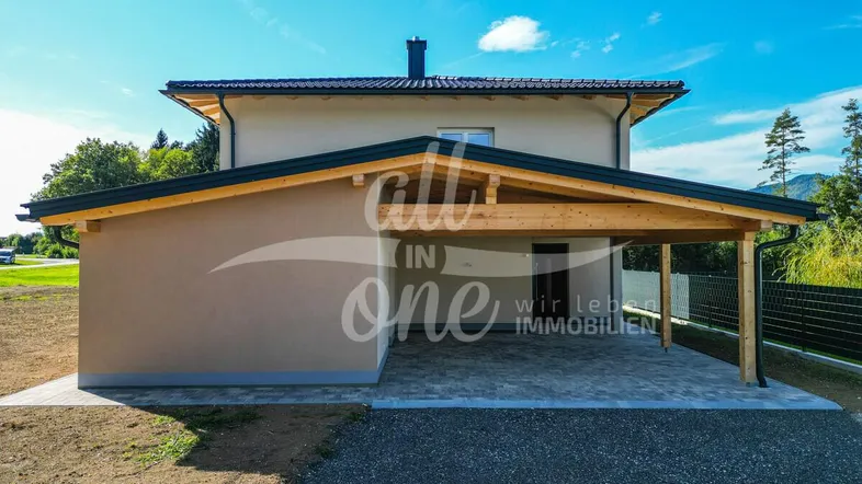Modernes Einfamilienhaus mit integriertem Carport und gepflasterter Zufahrt, umgeben von Natur.