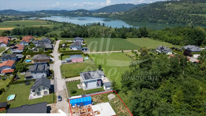Luftaufnahme eines Grundstücks mit im Bau befindlichem Haus und Seeblick in der Ferne.