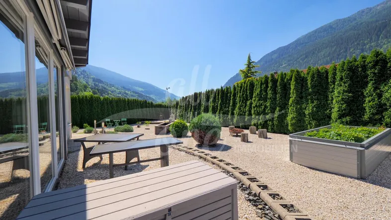 Sonniger Terrassenbereich mit Gartenmöbeln, Hochbeeten und Blick auf den gepflegten Garten.