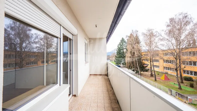 Langer Balkon mit Fliesenboden und Blick auf die Umgebung sowie ein Schulgebäude.