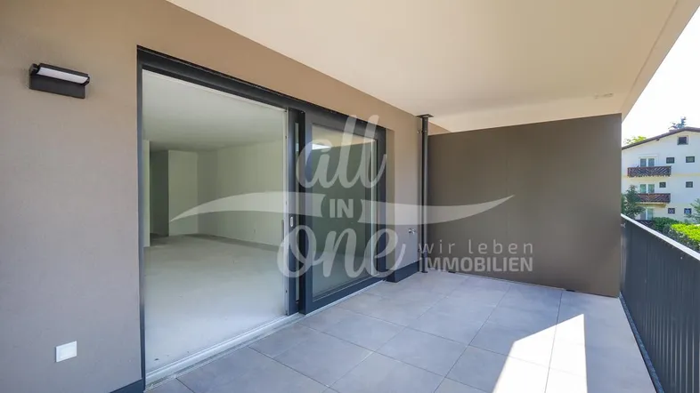 Geräumiger Balkon mit Fliesenboden und Schiebetüren, die zu einem leeren Innenraum führen.