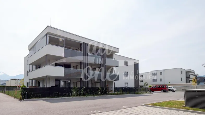 Modernes Mehrfamilienhaus mit Balkonen und Parkplätzen in einer ruhigen Wohngegend mit Bergblick.