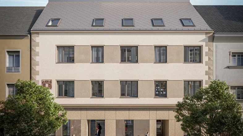 Moderne Fassade eines Wohngebäudes mit Mansarddach und belebter Straße davor.