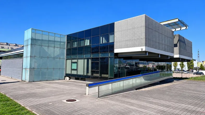 Modernes Bürogebäude mit Glasfassade und Rampe für barrierefreien Zugang unter blauem Himmel.