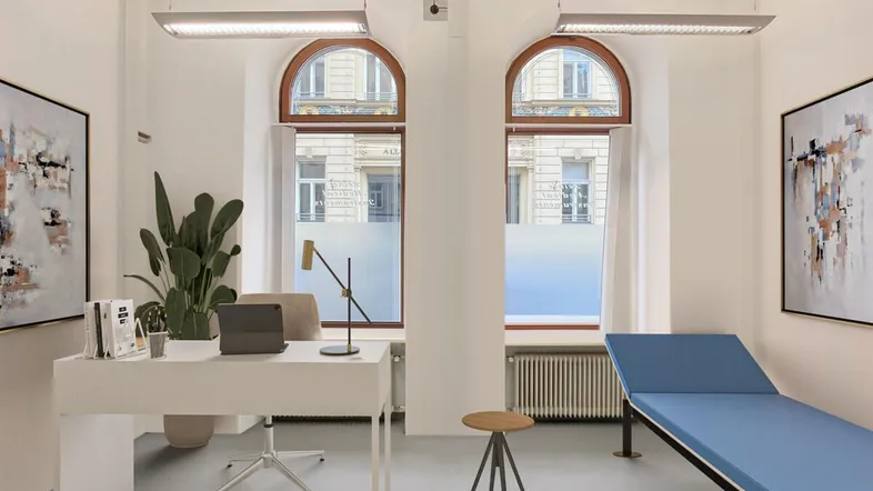 Heller Gewerberaum, virtuell als Büro oder Behandlungszimmer eingerichtet, mit großen Rundbogenfenstern und Heizkörpern.
