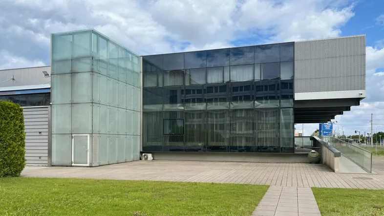 Modernes Geschäftsgebäude mit Glasfassade und Rampe, umgeben von Grünflächen unter bewölktem Himmel.