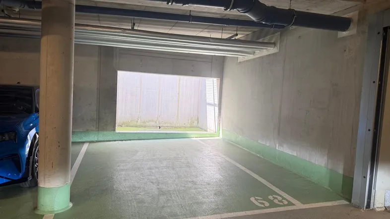 Tiefgaragenstellplatz mit Betonwänden, sichtbaren Rohren und grünen Bodenmarkierungen, teilweise beleuchtet.