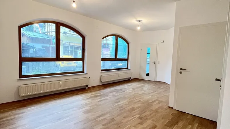 Helles Wohnzimmer mit Holzboden und zwei großen Rundbogenfenstern, die viel Tageslicht hereinlassen.