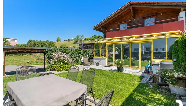 Sonniger Gartenbereich mit Terrasse, Gartenmöbeln und angrenzendem Wintergarten am Haus.